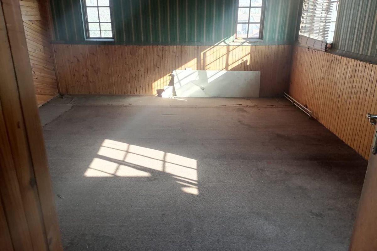 An empty bedroom featuring timber wall paneling and casement windows, requiring cosmetic updates and flooring replacement.