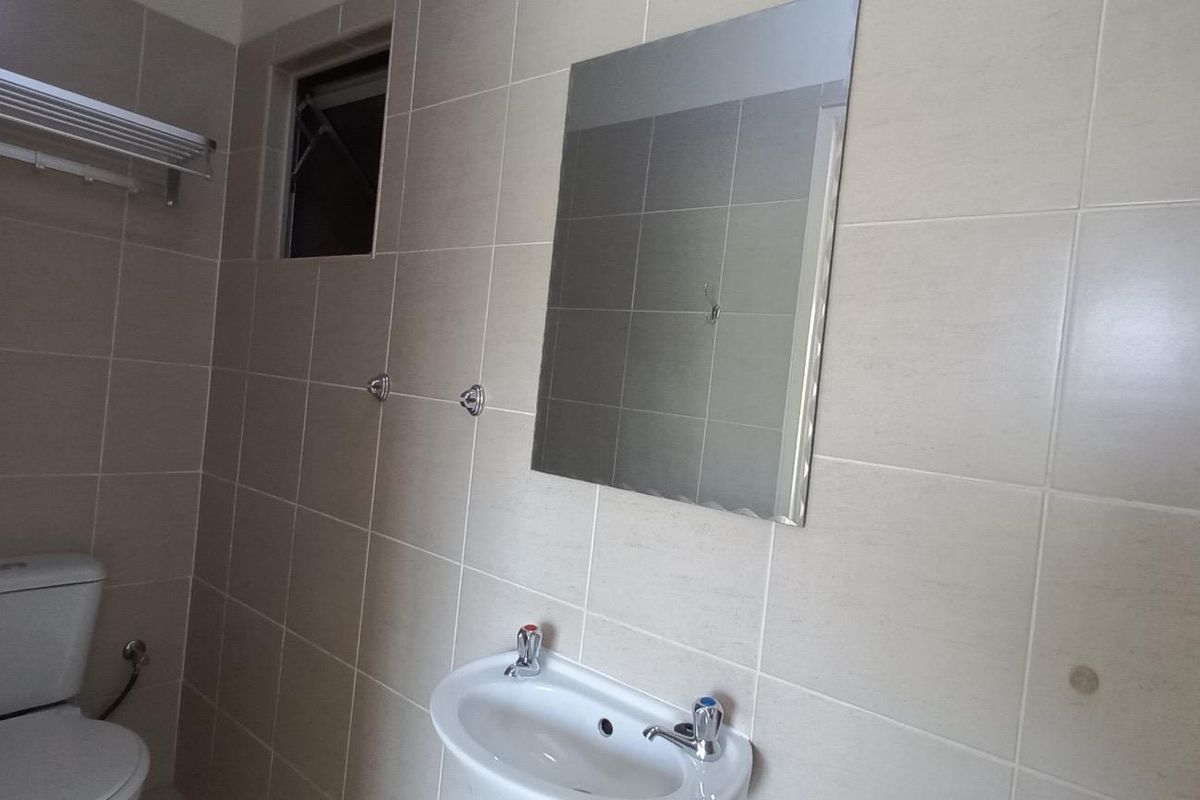 A clean, tiled bathroom featuring a pedestal basin, toilet, wall-mounted mirror, and towel rack, presenting a functional and well-maintained space.