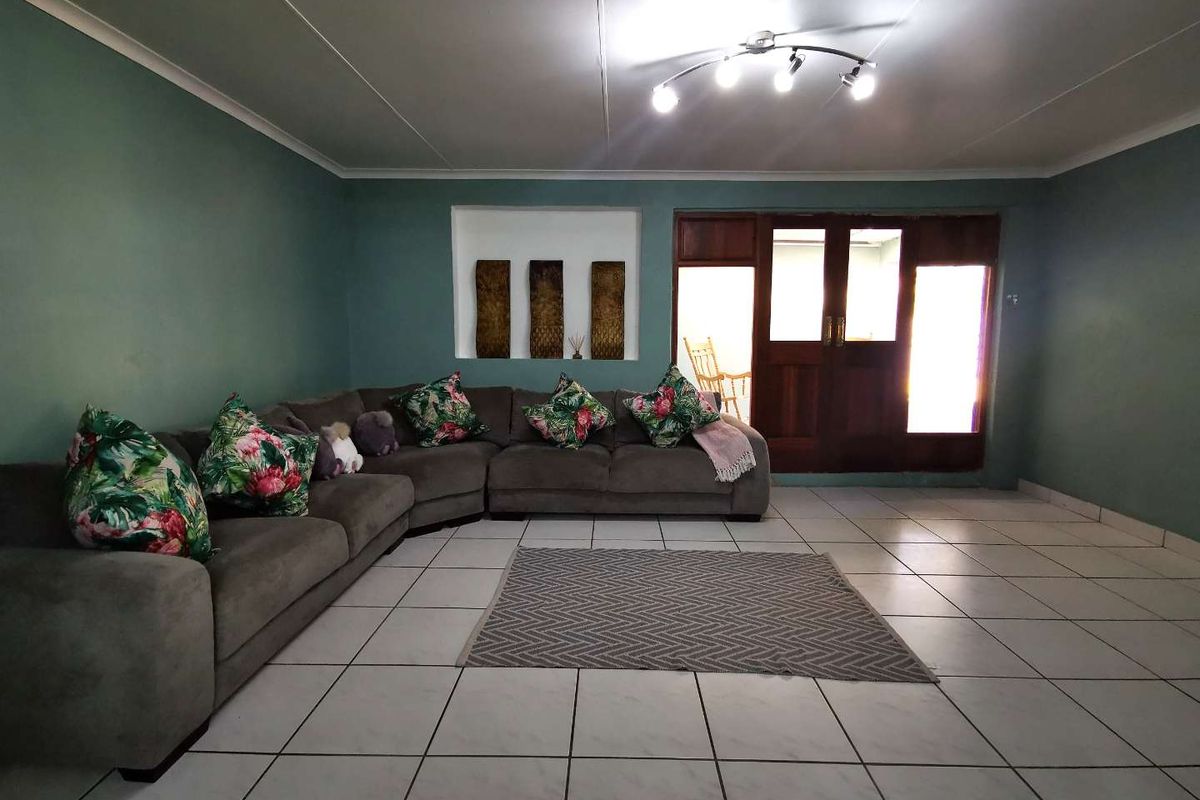 Spacious living room featuring tiled flooring, a recessed wall niche, and wooden framed glass doors leading to an adjacent area.