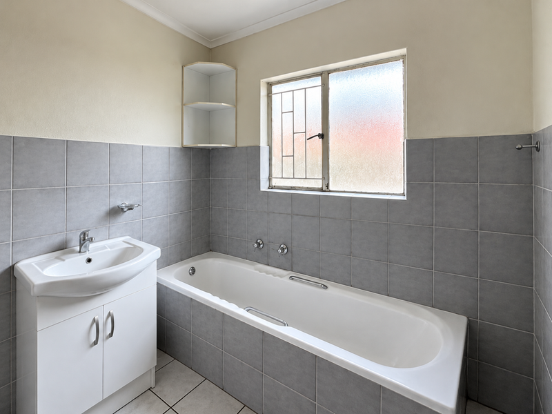 A functional bathroom featuring a built-in vanity with basin, a bathtub with tiled surround, and neutral grey wall tiling.