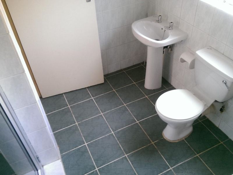 A functional bathroom featuring a pedestal basin, toilet, and shower enclosure with tiled walls and flooring.
