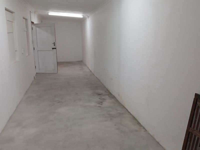 A long, empty industrial hallway featuring concrete flooring, white walls, and basic fluorescent lighting, suitable for storage or utility use.