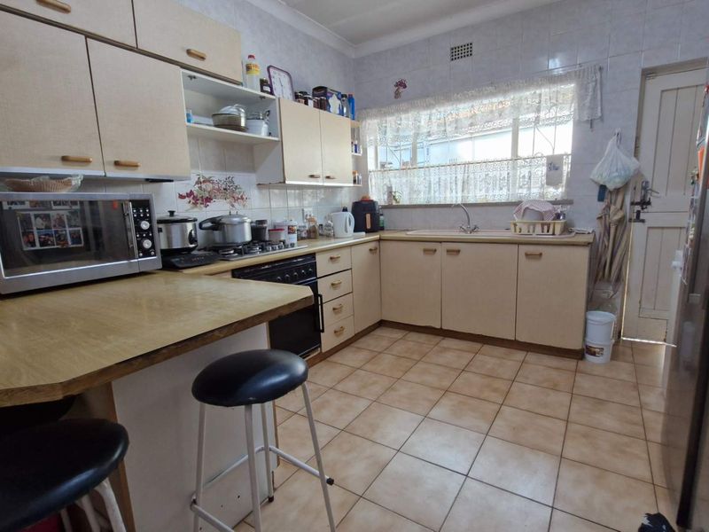 A functional kitchen featuring tiled flooring, ample built-in cabinetry, a gas hob, and a double sink with a tiled backsplash.