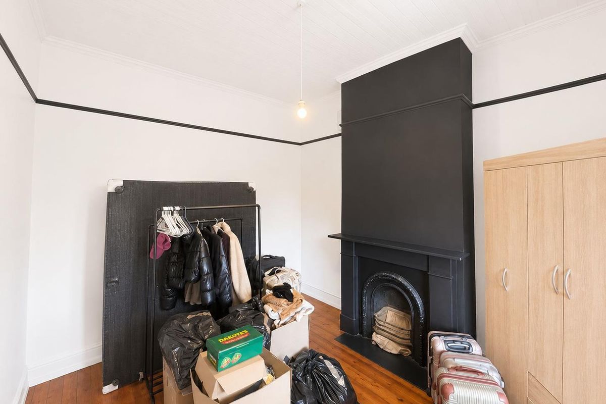 A bedroom featuring original timber flooring, a decorative fireplace with a black mantle, and classic picture rails.