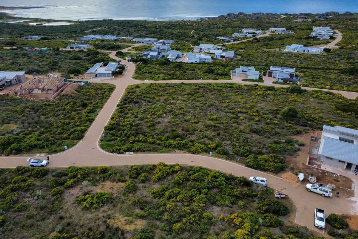 Aerial view of a residential estate featuring paved roads, natural coastal vegetation, and surrounding homes near the ocean.