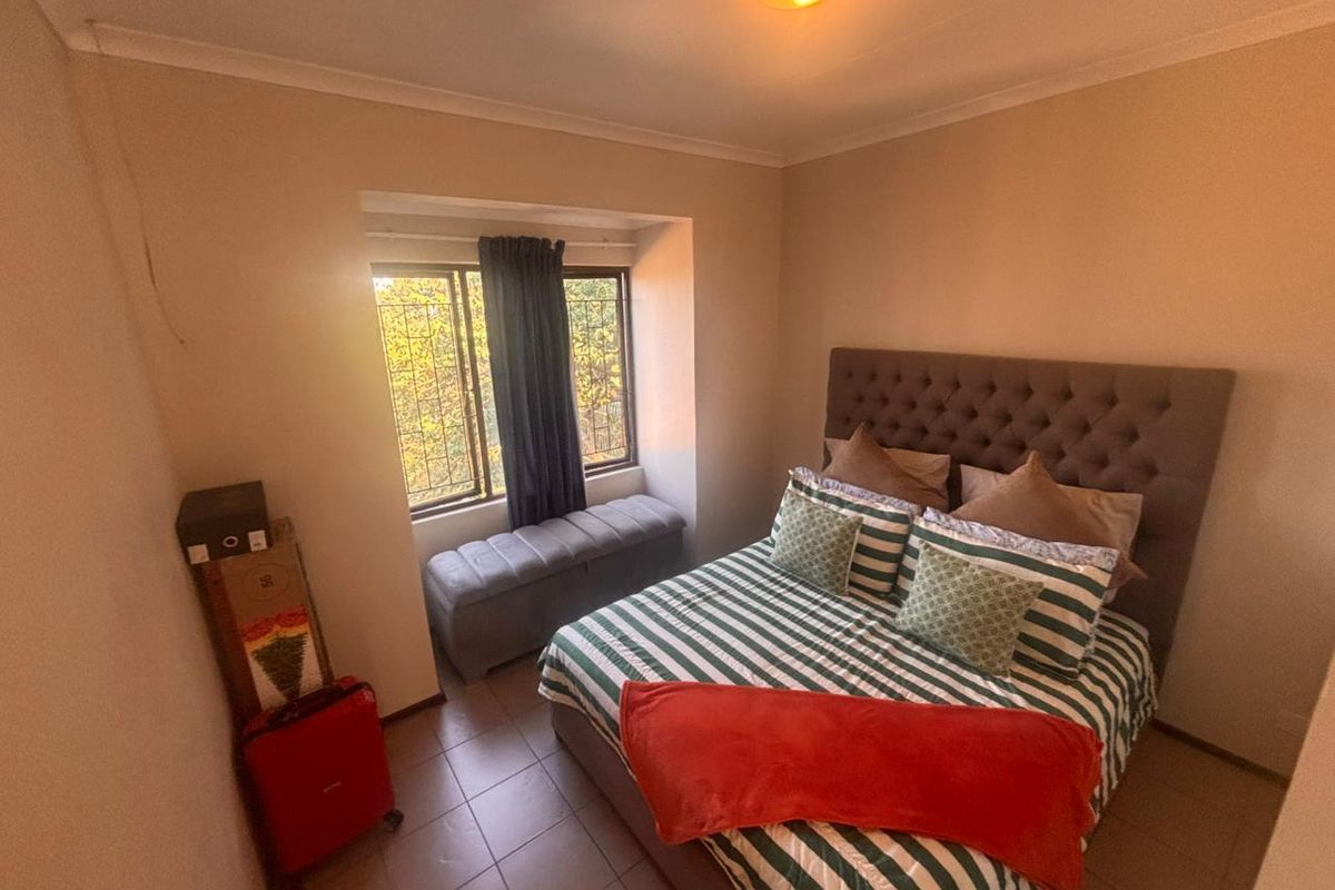 A cozy bedroom featuring tiled flooring, a recessed window with security bars, and a neutral color palette.