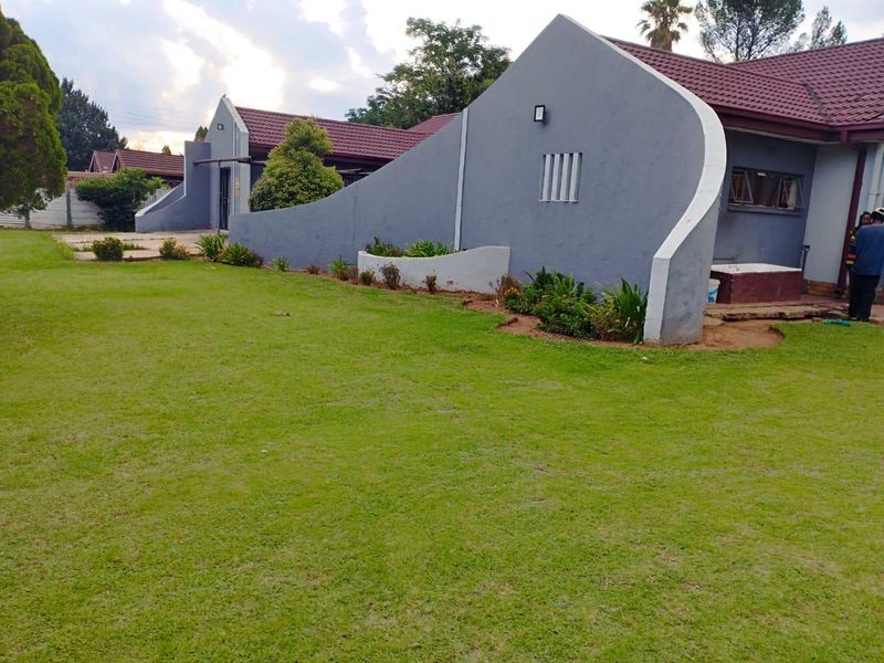 A view of the rear exterior of the house featuring a large lawn, a distinctive curved feature wall, and a tiled roof.