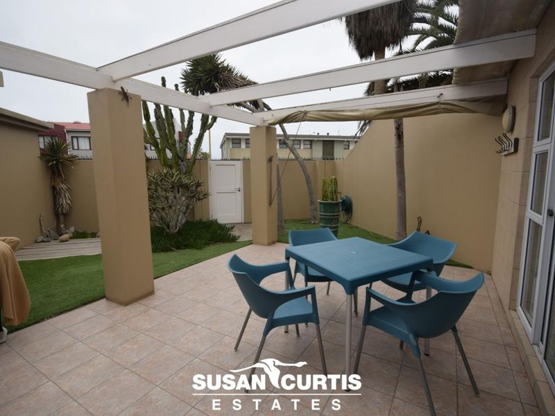A covered patio area featuring tiled flooring, a pergola structure, and a small enclosed garden space with artificial grass and boundary walls.
