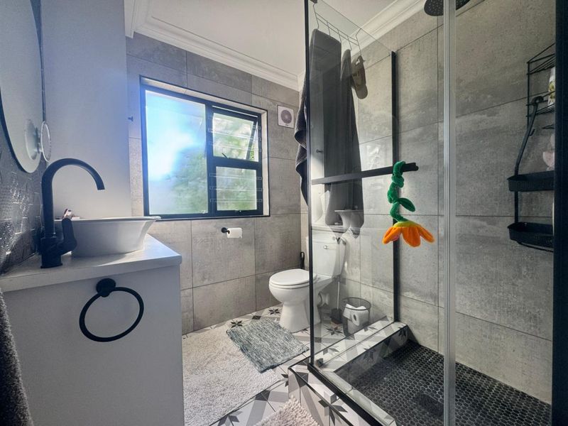 Modern bathroom featuring a glass shower enclosure, vessel sink with matte black fixtures, and contemporary grey wall and patterned floor tiling.