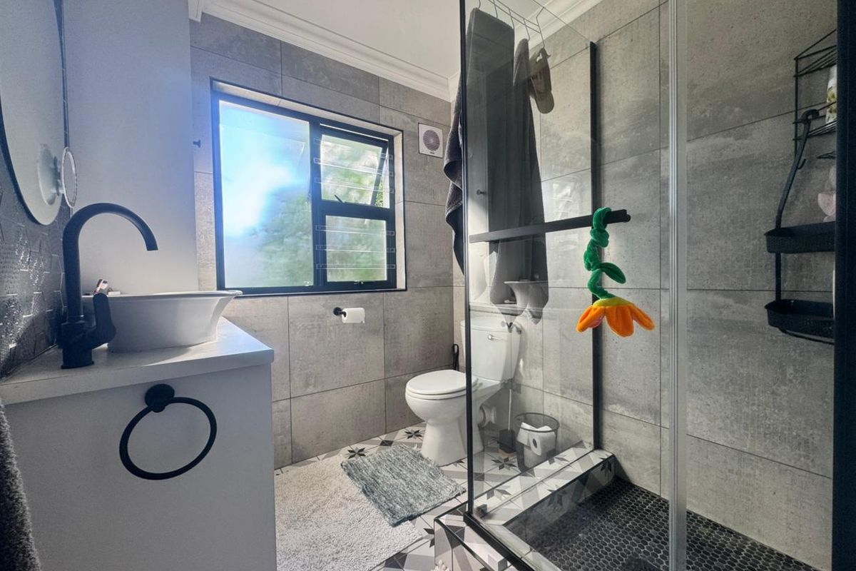 Modern bathroom featuring a glass shower enclosure, vessel sink with matte black fixtures, and contemporary grey wall and patterned floor tiling.