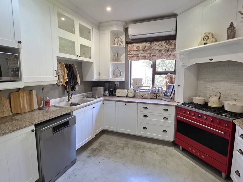 A well-appointed kitchen featuring white cabinetry, granite countertops, a double basin sink, and a distinctive red Smeg range cooker with an integrated extractor hood.