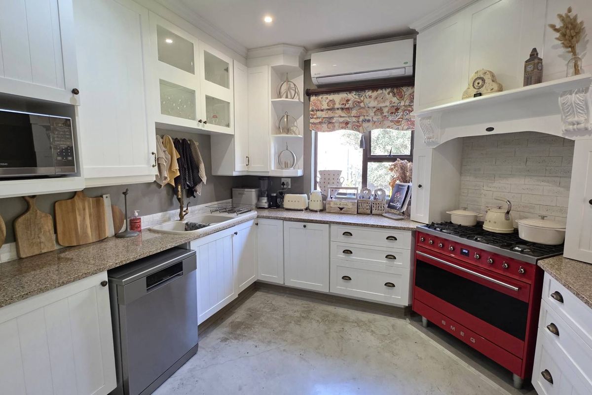 A well-appointed kitchen featuring white cabinetry, granite countertops, a double basin sink, and a distinctive red Smeg range cooker with an integrated extractor hood.