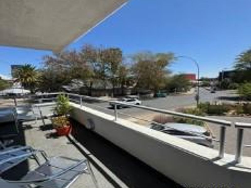 An elevated balcony featuring a metal railing and concrete flooring, offering an open view of the surrounding street and neighborhood.