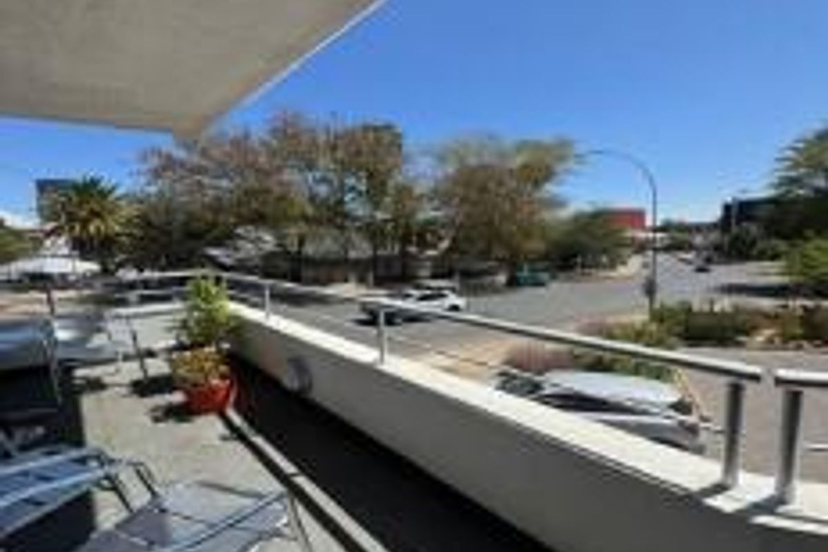 An elevated balcony featuring a metal railing and concrete flooring, offering an open view of the surrounding street and neighborhood.
