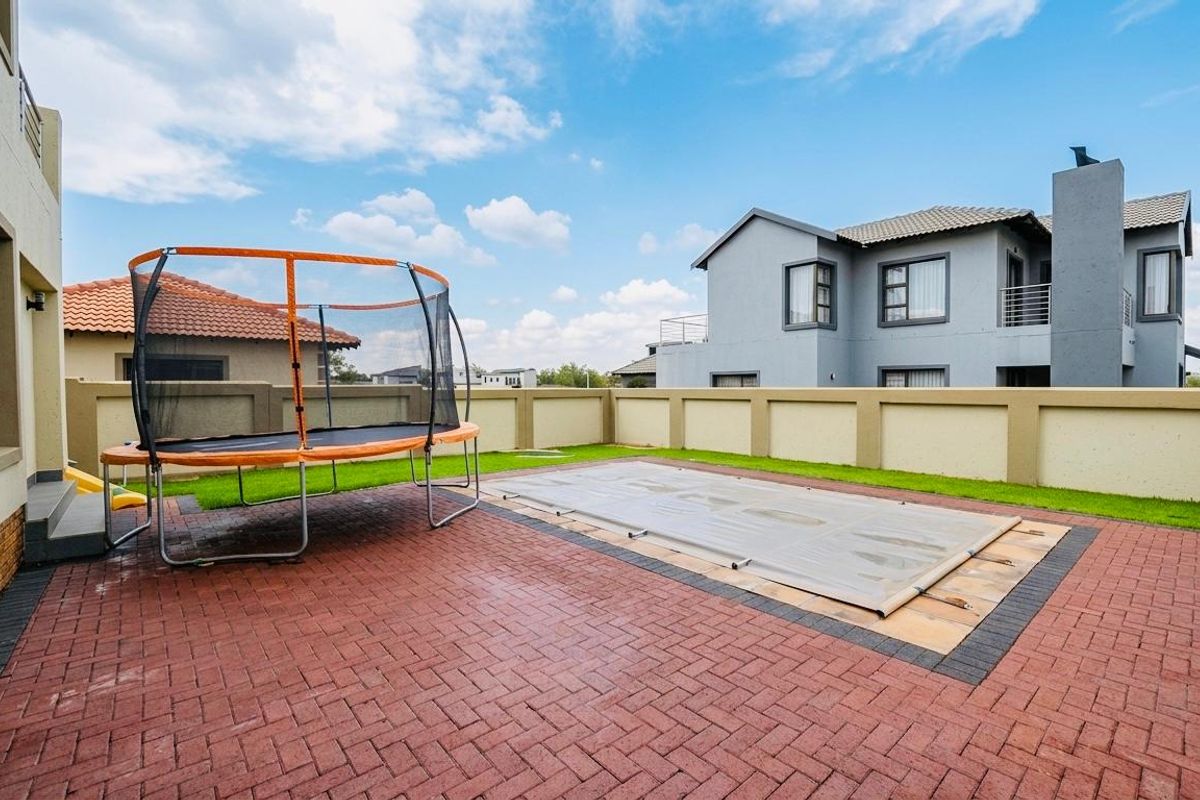 A private rear garden featuring a paved patio area, a swimming pool with a safety cover, and perimeter boundary walls.