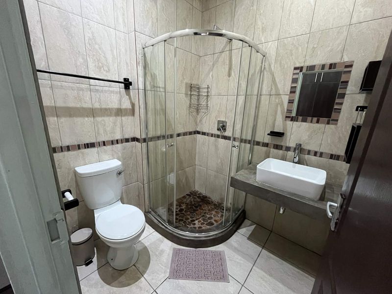 A compact bathroom featuring a corner shower enclosure with pebble flooring, a wall-mounted basin, and neutral wall tiling.