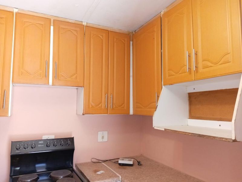 A dated kitchen area featuring wooden cabinetry, a laminate countertop, and a freestanding stove, currently requiring minor finishing work and cosmetic updates.