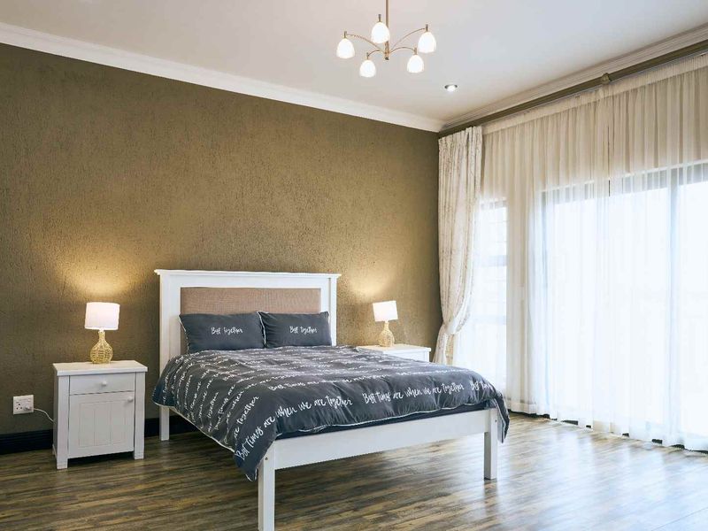 A spacious bedroom featuring laminate flooring, a textured accent wall, and large sliding glass doors that provide ample natural light.