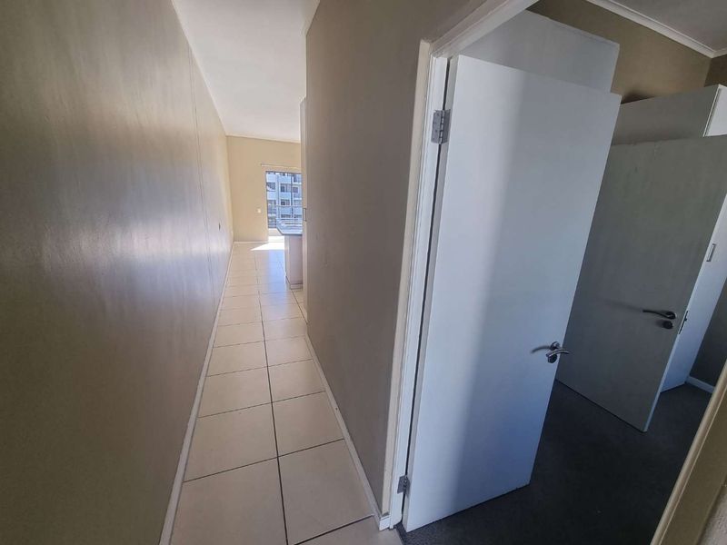 A neutral-toned hallway with tiled flooring, providing access to adjacent rooms and leading towards an open-plan living area.