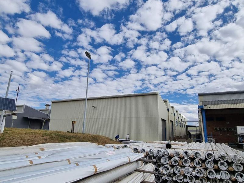 Exterior view of an industrial facility featuring metal cladding, high-mast lighting, and a solar panel installation within a paved yard area.