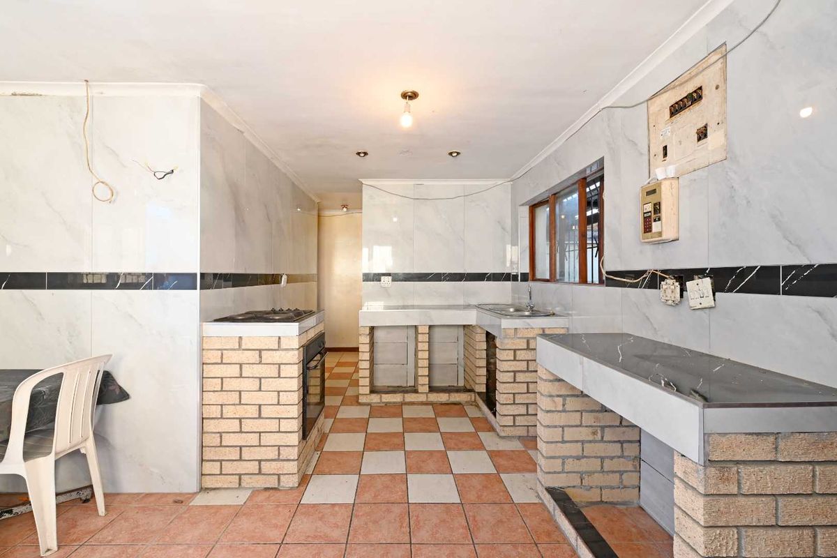 A dated kitchen featuring brick-built cabinetry, tiled surfaces, and exposed electrical wiring, offering significant potential for a modern renovation and layout update.