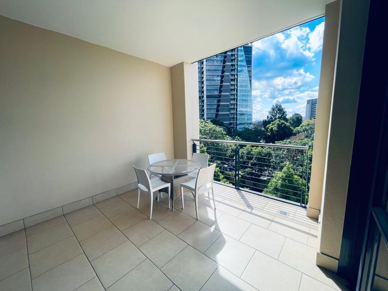 A spacious covered balcony featuring tiled flooring and a modern stainless steel balustrade, offering pleasant urban views.