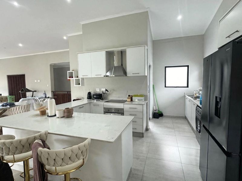 Modern open-plan kitchen featuring white cabinetry, quartz countertops, integrated appliances, and sleek tiled flooring, seamlessly connecting to the living area.