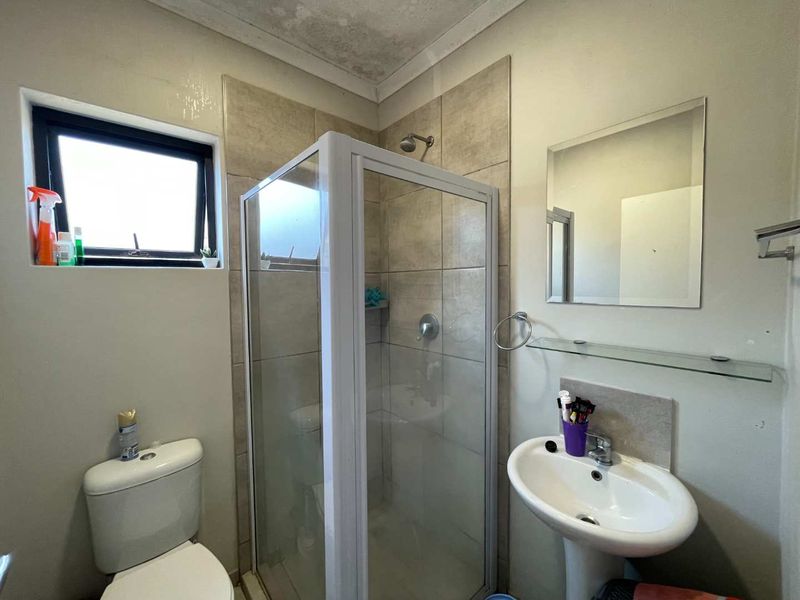 Compact bathroom featuring a shower enclosure, pedestal basin, and toilet, with visible ceiling water staining requiring attention.