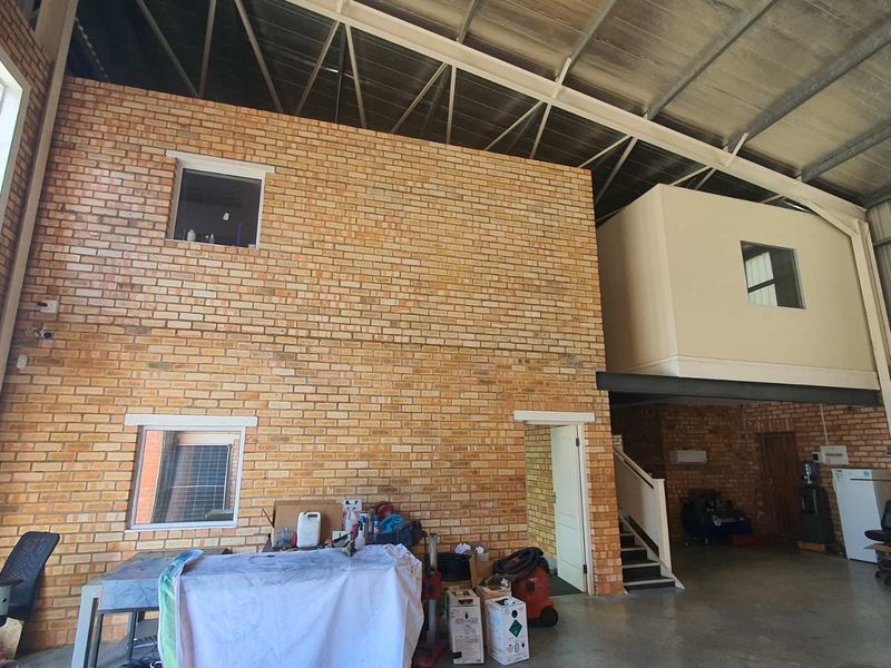 Spacious industrial utility area featuring high ceilings, exposed brickwork, and a mezzanine level, suitable for workshop or storage use.