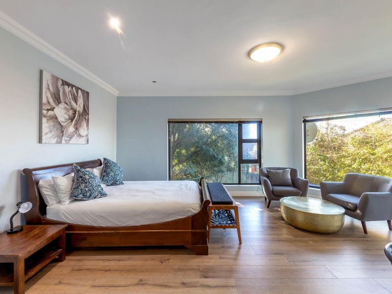 Spacious bedroom featuring laminate flooring, crown molding, and large windows providing ample natural light and garden views.