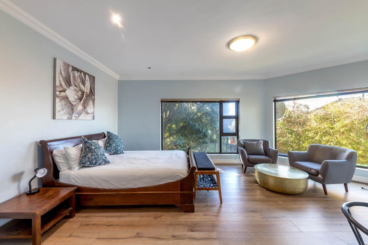 Spacious bedroom featuring laminate flooring, crown molding, and large windows providing ample natural light and garden views.