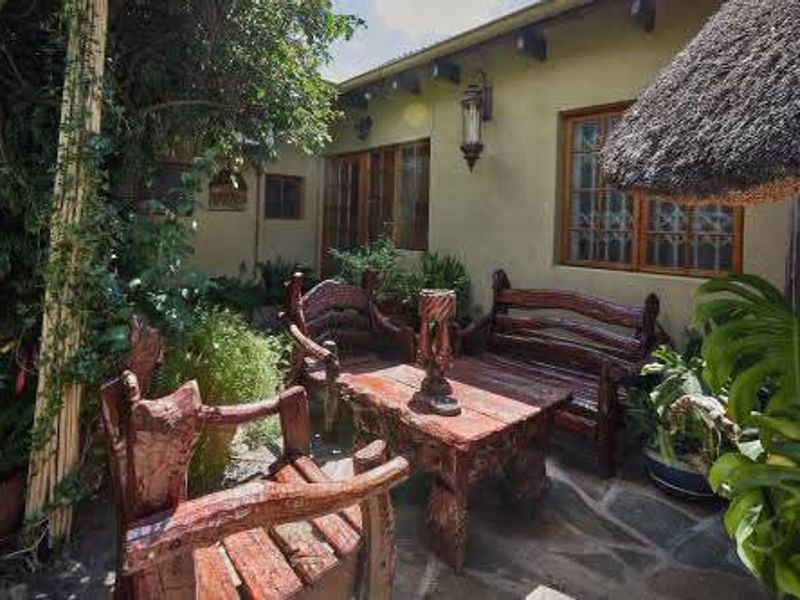 A charming covered patio area featuring stone paving, exposed timber beams, and a traditional thatched roof, creating a cozy outdoor seating space.