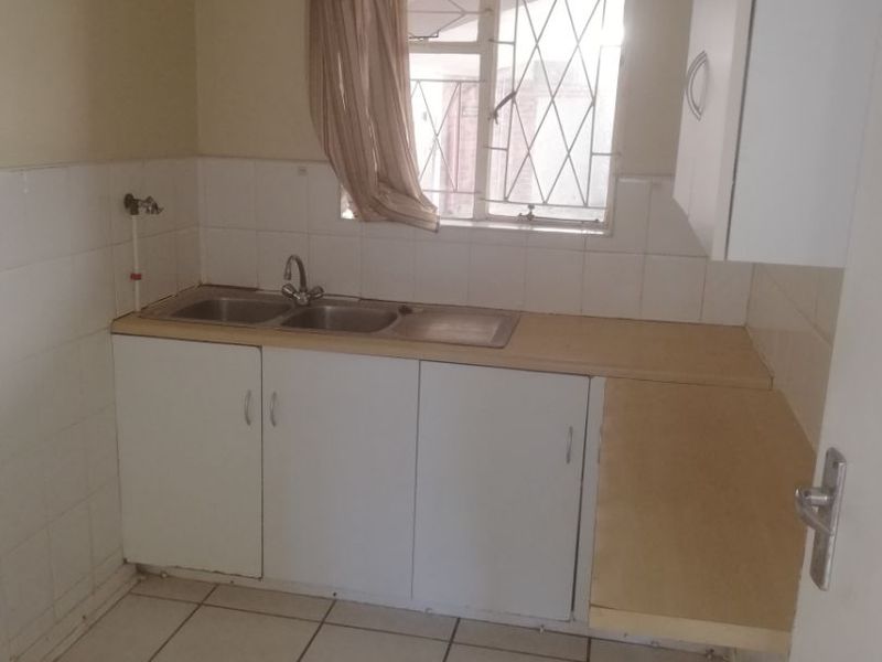 A compact kitchen featuring tiled flooring, a double sink with splashback, and basic built-in cabinetry, offering a functional space ready for modernization.