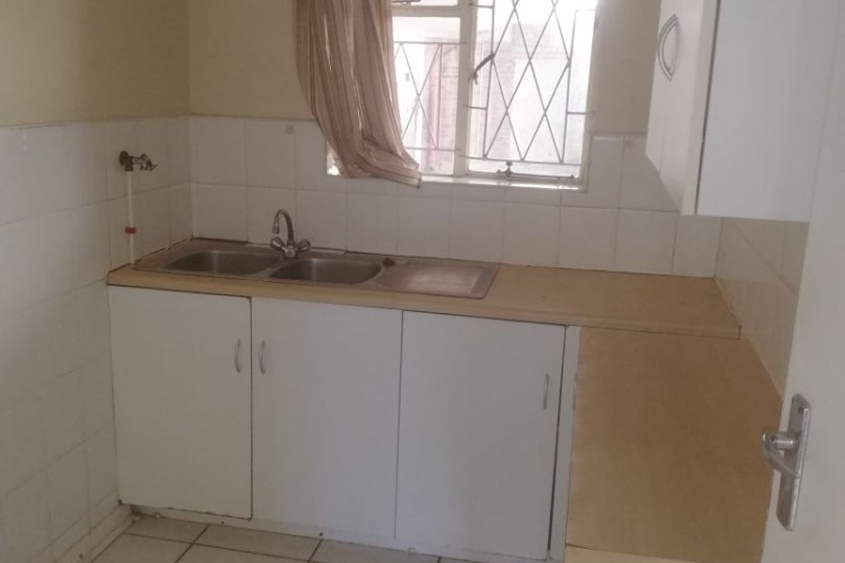 A compact kitchen featuring tiled flooring, a double sink with splashback, and basic built-in cabinetry, offering a functional space ready for modernization.