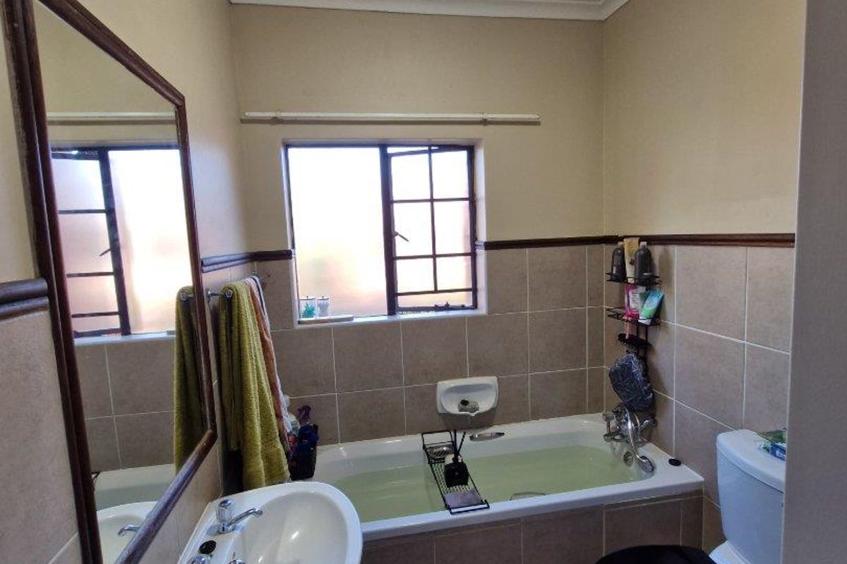 A functional bathroom featuring a pedestal basin, a bathtub with tiled surround, and a toilet, finished with neutral wall tiles and a window.