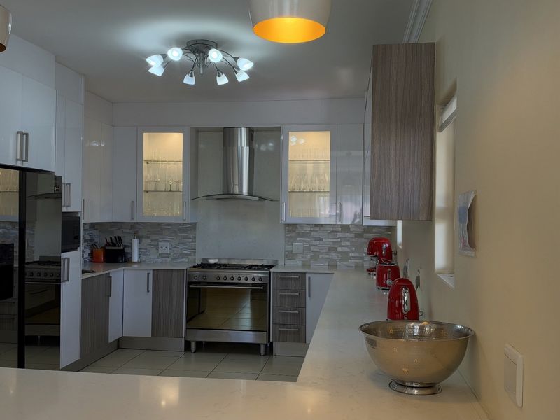 Modern kitchen featuring white and wood-tone cabinetry, stone countertops, a gas stove with stainless steel extractor fan, and glass-fronted display cabinets.