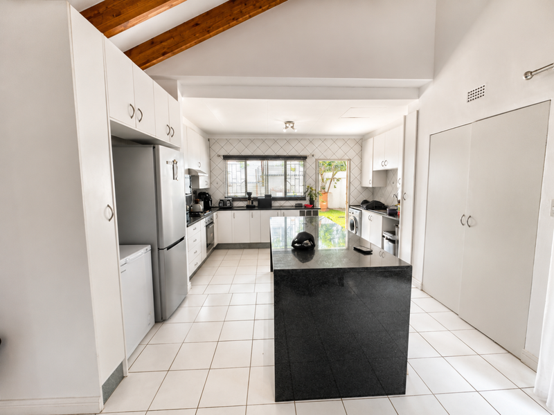 Spacious kitchen featuring a large central island with granite countertops, white cabinetry, tiled flooring, and exposed timber ceiling beams with direct outdoor access.