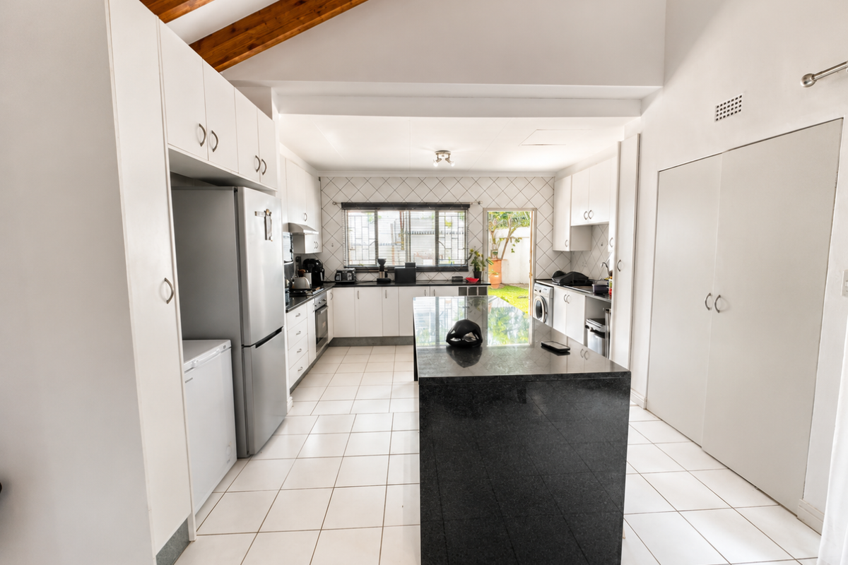 Spacious kitchen featuring a large central island with granite countertops, white cabinetry, tiled flooring, and exposed timber ceiling beams with direct outdoor access.