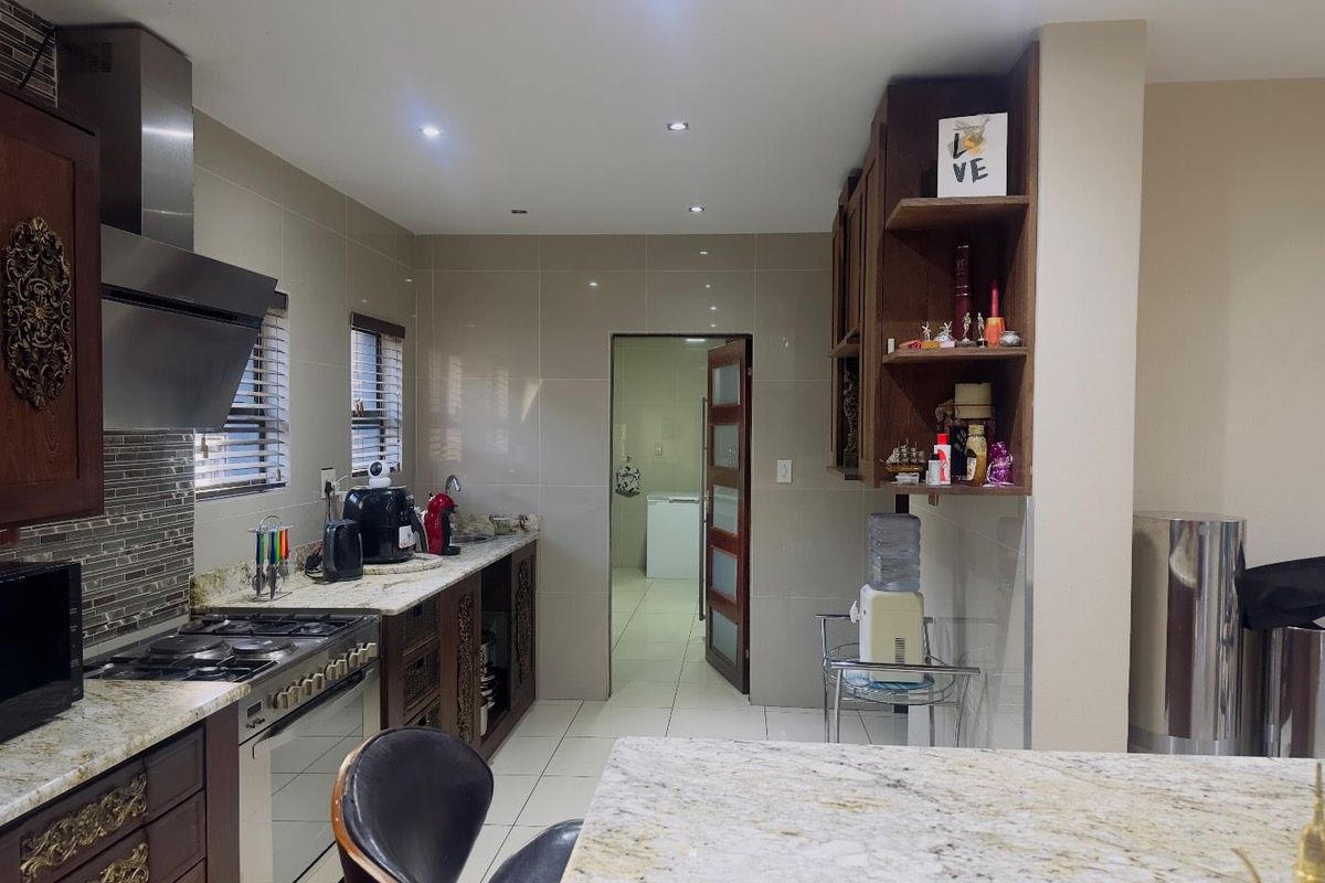 A functional kitchen featuring granite countertops, dark wood cabinetry, a stainless steel extractor fan, and a gas stove, with an adjacent scullery area.