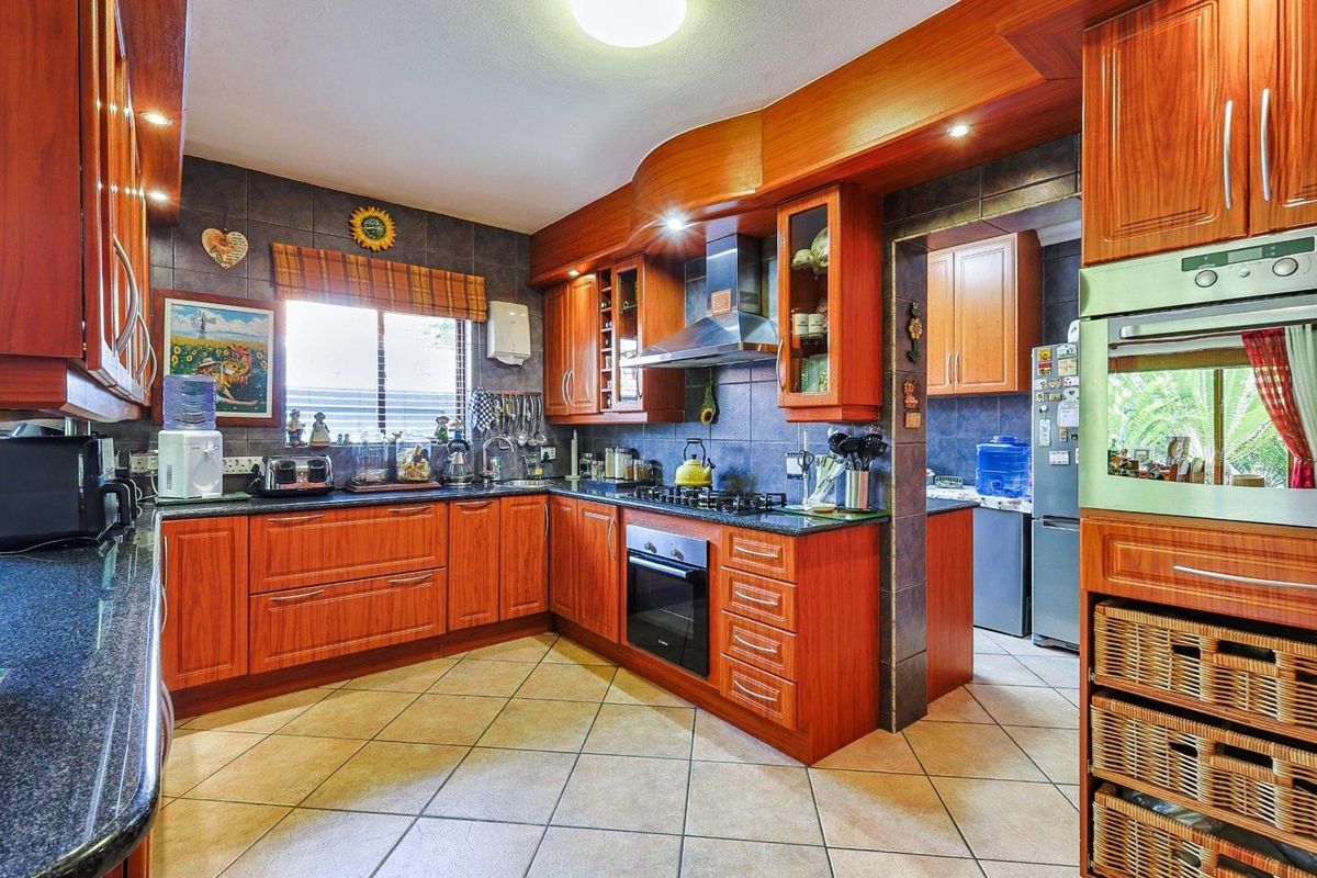 A functional kitchen featuring warm-toned wooden cabinetry, granite countertops, a built-in oven, gas hob, and tiled flooring with an adjacent scullery area.