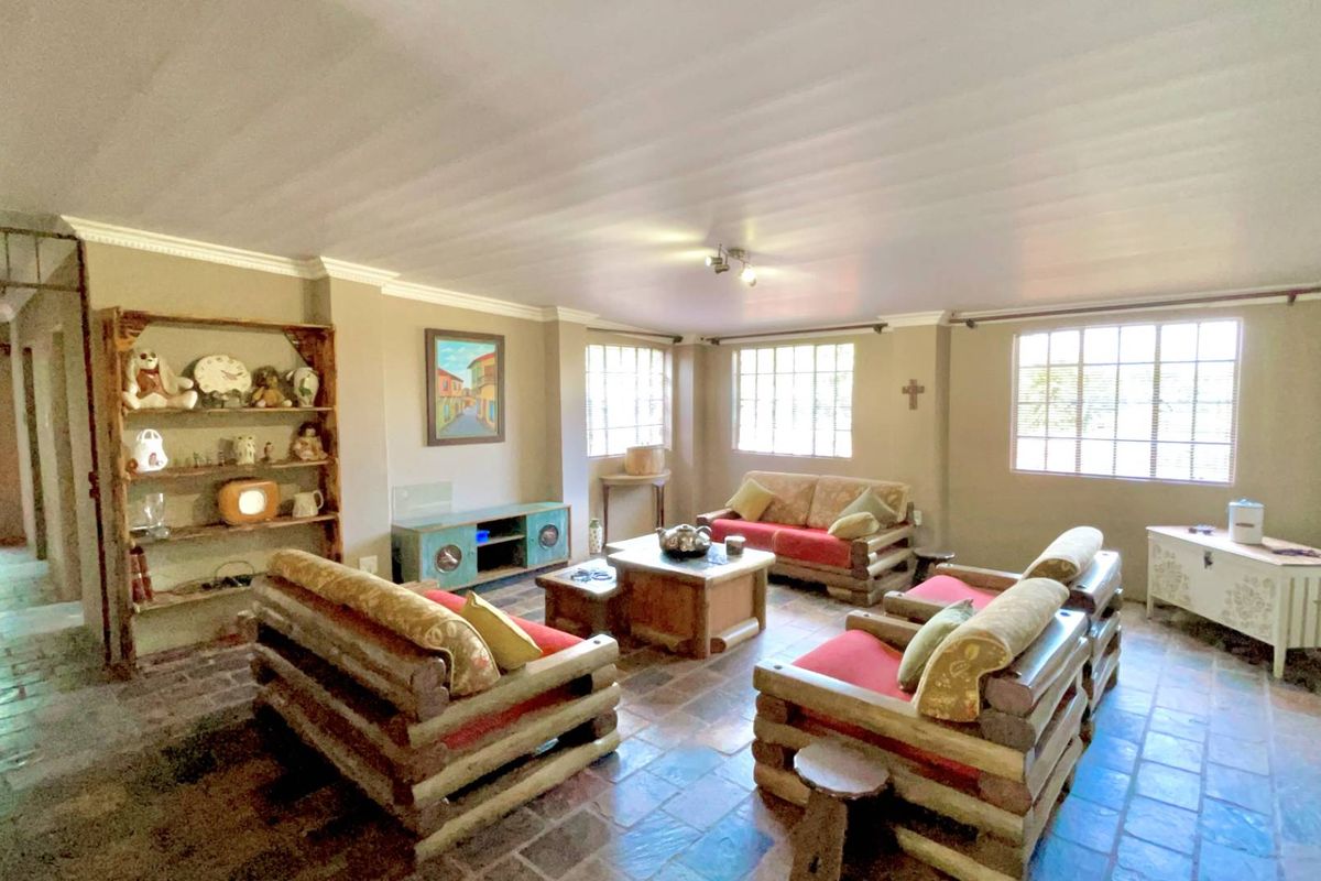 A spacious living room featuring rustic terracotta-style floor tiles, large windows providing natural light, and crown molding detail.