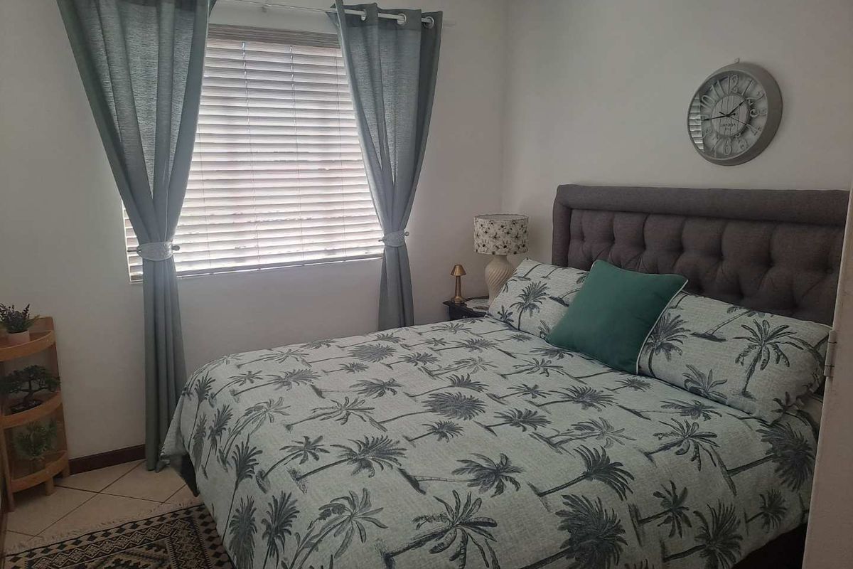 A cozy bedroom featuring tiled flooring, a window with fitted blinds, and neutral wall finishes.