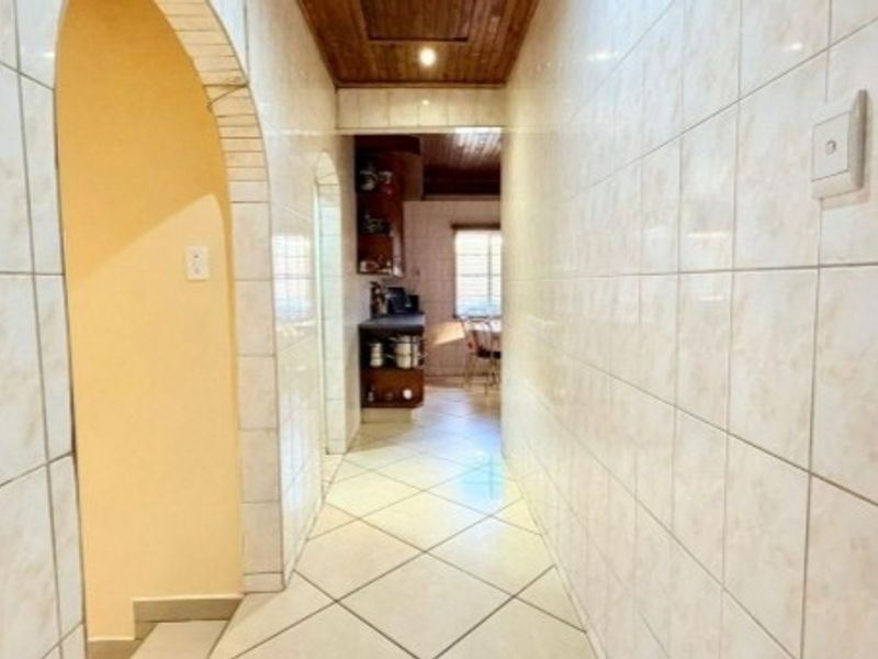 A tiled hallway featuring an arched entryway and timber ceiling, leading through to an adjacent living area.