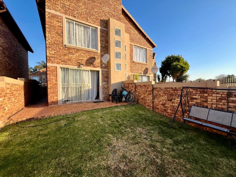 Rear view of a face brick townhouse featuring a private garden, paved patio area, and sliding door access to the interior living space.