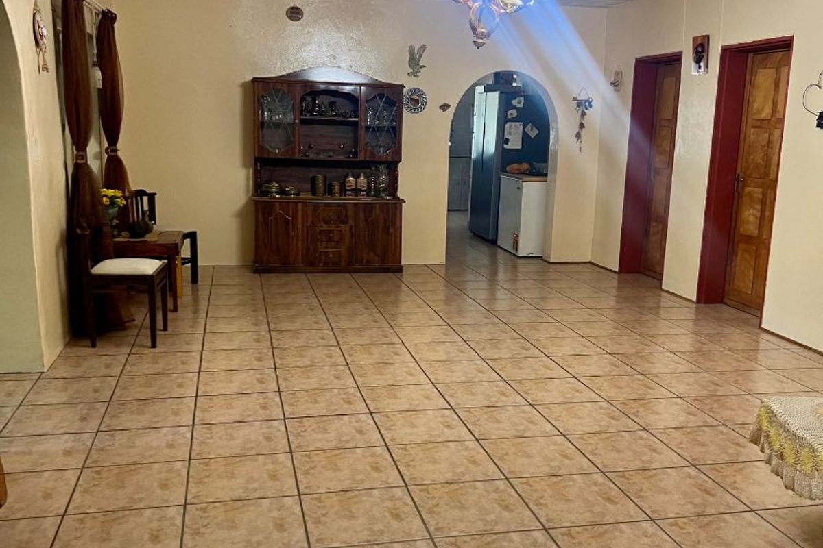 Spacious living area featuring ceramic floor tiles, a corrugated metal ceiling, and an arched entryway leading to the kitchen area.