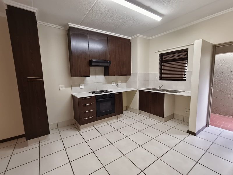 A clean, functional kitchen featuring dark wood cabinetry, built-in oven and hob, tiled flooring, and a double sink with a window view.