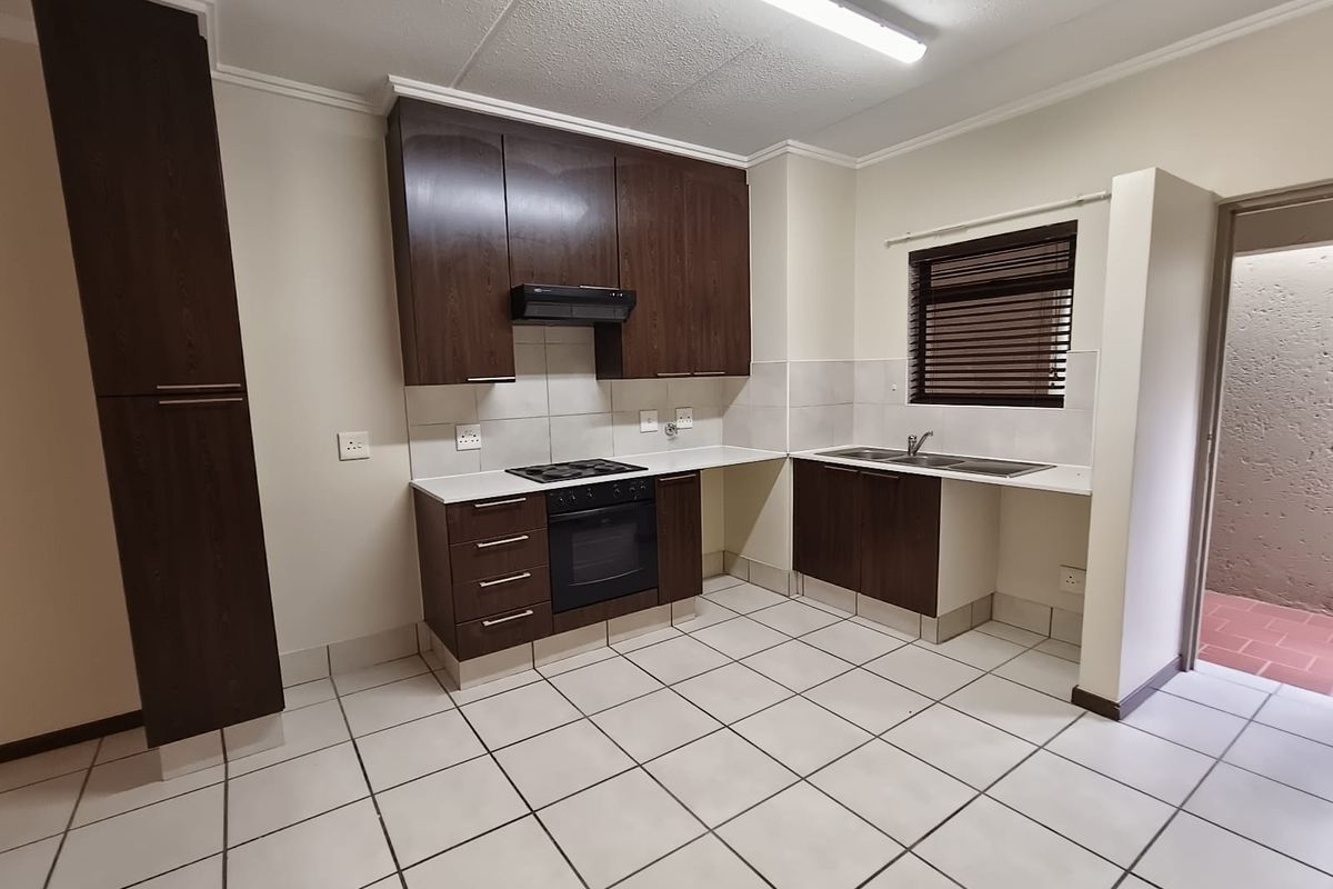 A clean, functional kitchen featuring dark wood cabinetry, built-in oven and hob, tiled flooring, and a double sink with a window view.