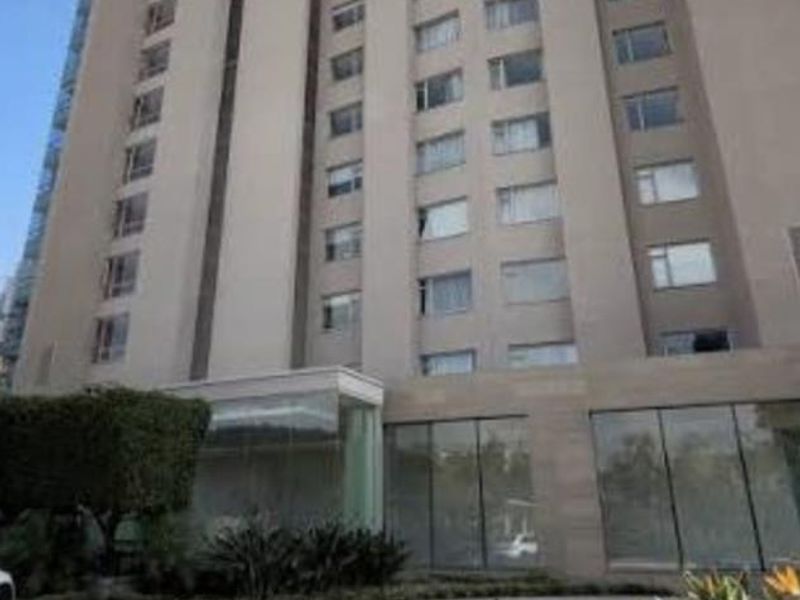 A low-angle view of a modern multi-story apartment building featuring a paved driveway entrance and landscaped garden beds.