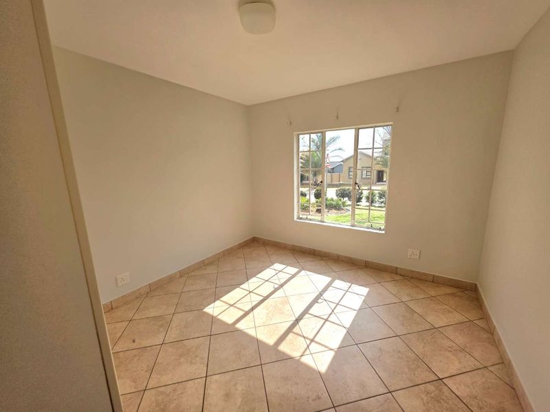An empty bedroom featuring neutral walls, tiled flooring, and a metal-framed window providing natural light.