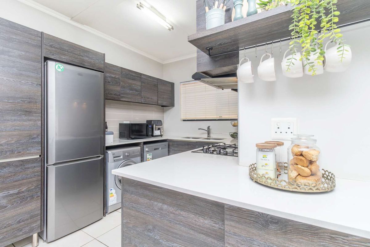 Modern kitchen featuring dark wood-grain cabinetry, stone countertops, a gas hob, extractor fan, and integrated laundry space with tiled flooring.